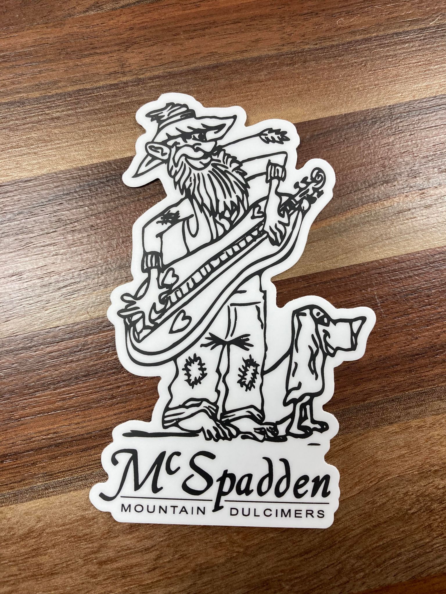 Sentence with product name: McSpadden Stickers depicting a caricature of a bearded figure with a mountain dulcimer and a dog, perfect for decorating laptops.