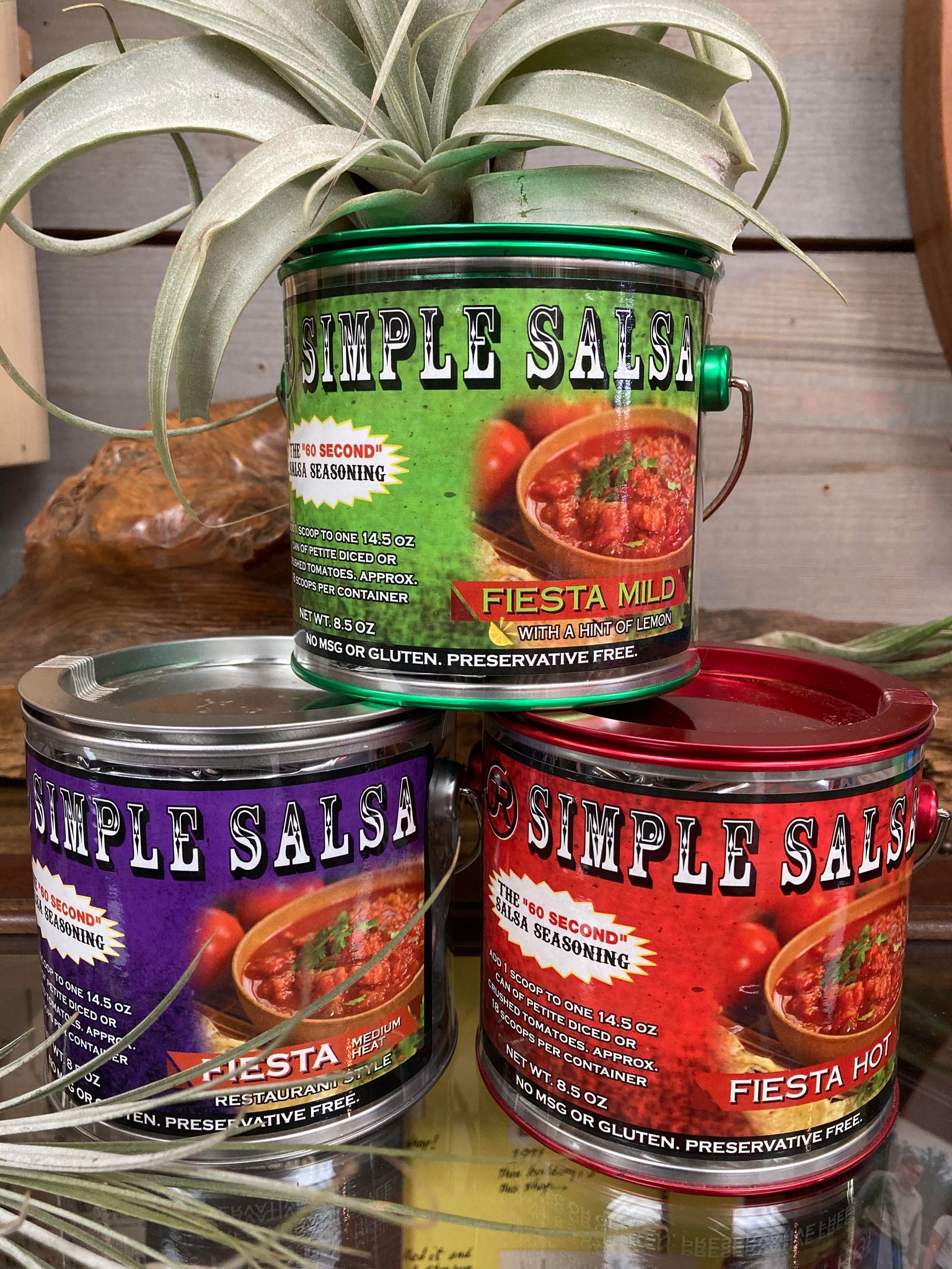Three colorful cans of Simple Salsa with a plant on top of the uppermost can, arranged on a wooden surface.