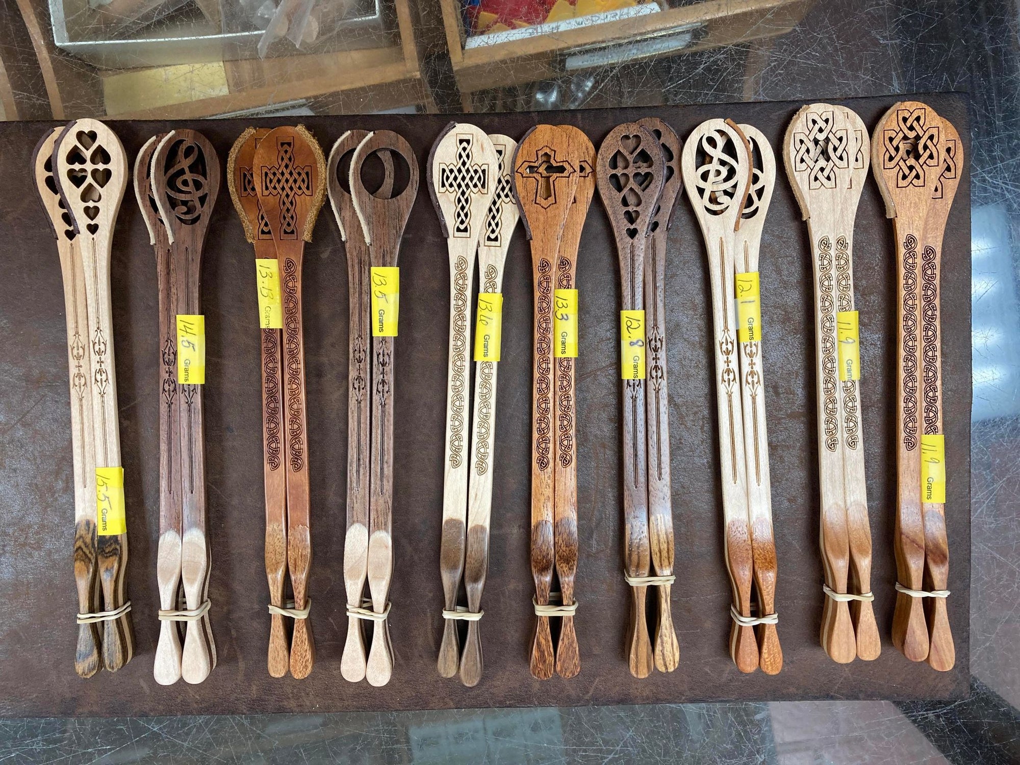 A collection of twelve intricately carved Master Works Hammer Dulcimer Hammers with various designs displayed on a wooden surface, each with a yellow price tag.