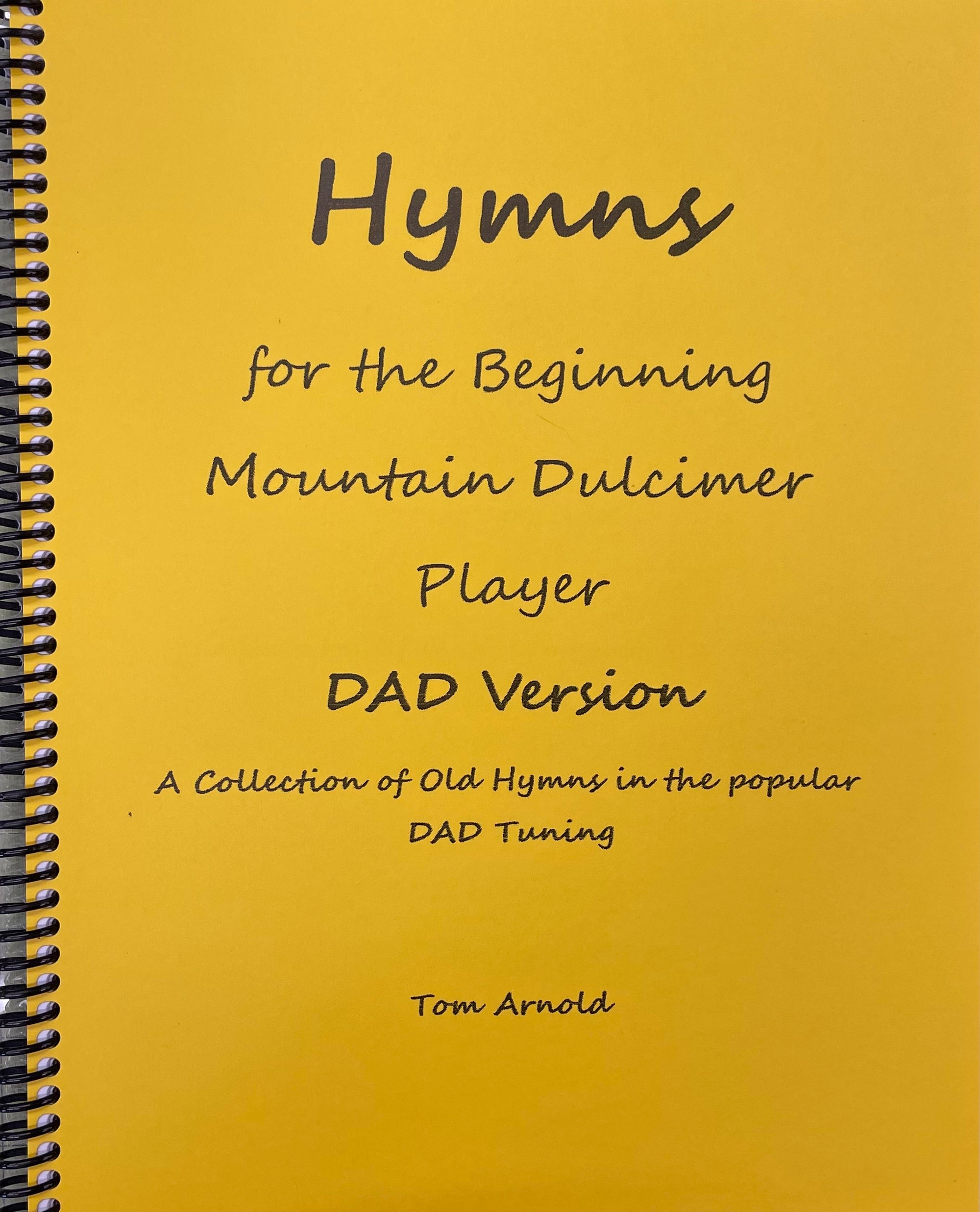 Spiral-bound yellow book cover titled "Hymns for the Beginning Mountain Dulcimer Player (DAD) by Tom Arnold," described as a collection of old hymns in DAD tuning with clear musical notation.
