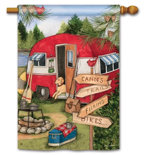 A painting of a red and white camper near a lake, with a yellow dog by the door, surrounded by camping gear and a flag pole displaying Studio M - Standard House Flag. A signpost points to canoes, trails, fishing, and bikes.