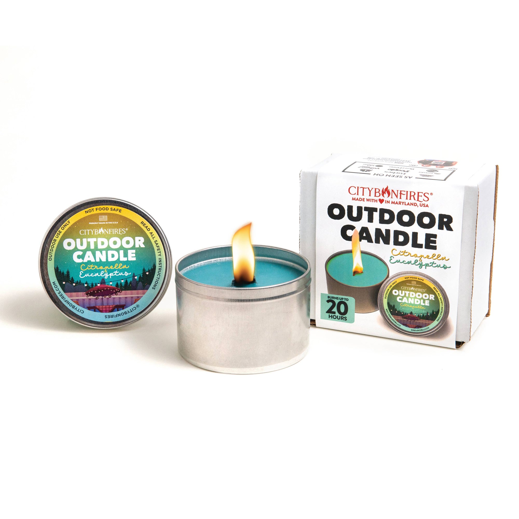 An eco-friendly outdoor candle in an open metal tin is lit, with an additional closed tin and a packaged candle box displayed beside it on a white background. The Outdoor Candle - Citronella and Eucalyptus