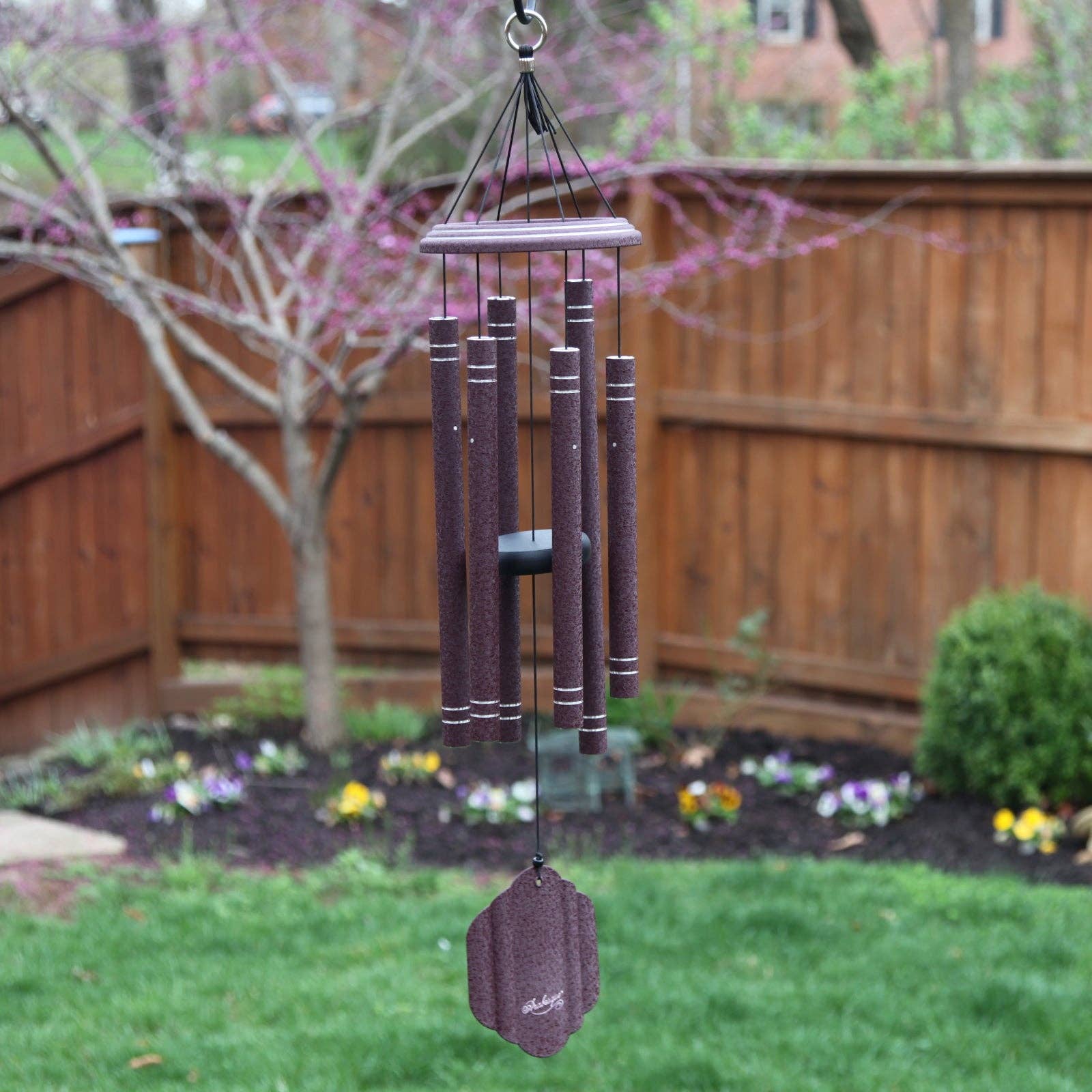 An intricately designed 32" Windchime Arabesque® hanging from a fence in a serene backyard, producing high-quality sound.