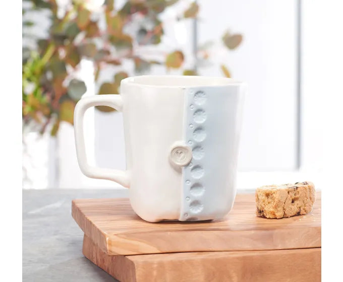 A handmade ceramic mug from the Studio M Coffee Mugs collection, featuring a unique button design in blue and white.