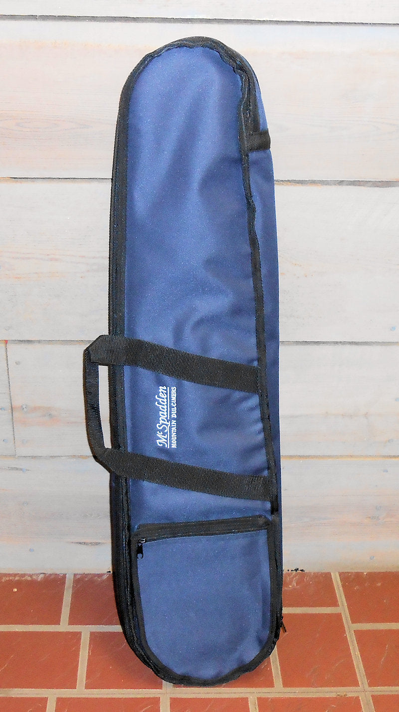 A navy nylon Standard Case with black trim and a logo on the side, standing upright against a brick and wooden wall.