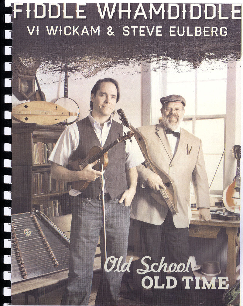 Two musicians posing with their instruments, a Fiddle Whamdiddle Old School Old Time by Steve Eulberg and Vi Wickam and a hammer dulcimer, in a room filled with books including a music book and a globe.