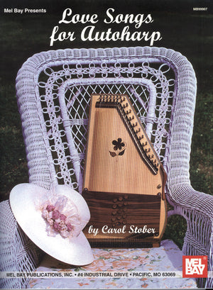 A wicker chair holds an autoharp, a wide-brimmed hat with flowers, and sheet music with complete lyrics. The text reads "Love Songs for the Autoharp by Carol Stober," showcasing the Mel Bay Publishing logo.