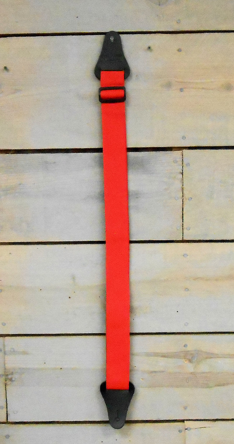 An adjustable Nylon Strap - Red with notched ends hanging on a wooden wall.