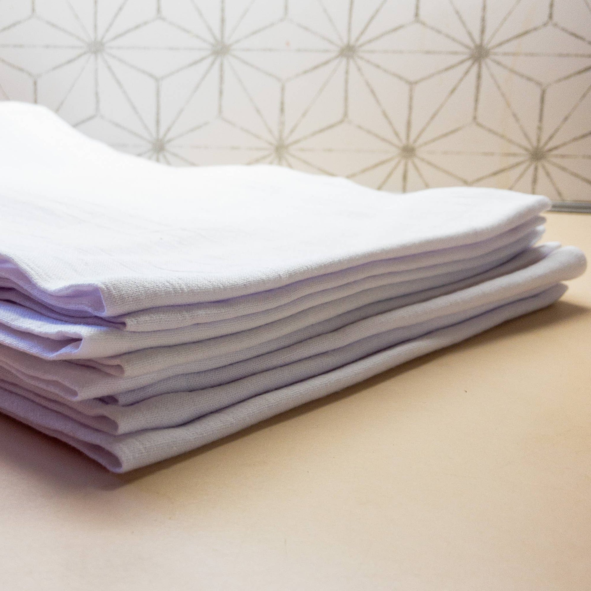 A stack of neatly folded white and light purple towels, including a Funny Chicken Tea Towel with heat transfer vinyl, on a countertop.