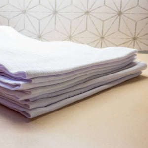 A stack of neatly folded white and light purple towels, including a Funny Chicken Tea Towel with heat transfer vinyl, on a countertop.