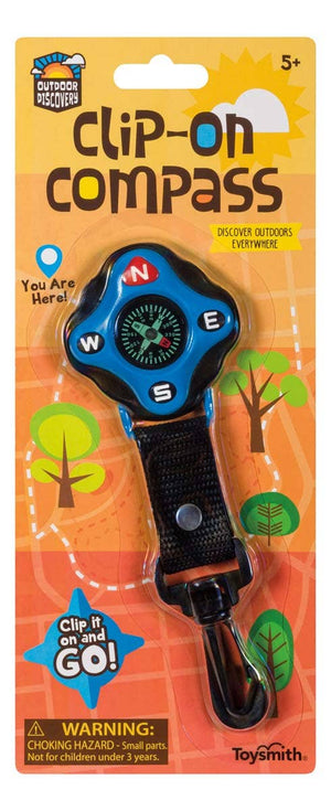 A packaged Outdoor Discovery Backyard Exploration Clip-On Compass, featuring a carabiner clip and labeled for ages 5 and up, with decorative background.