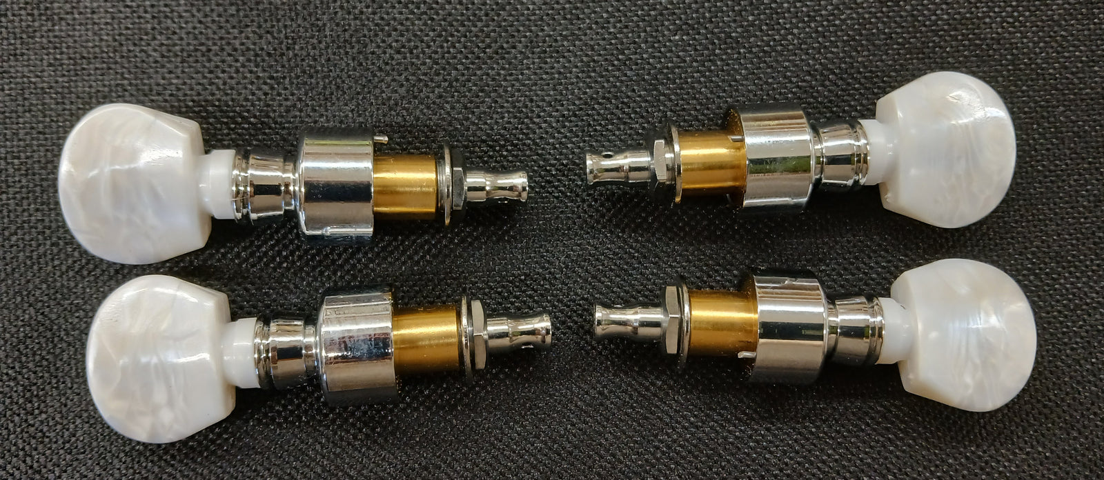 A set of four Planetary Tuning Pegs - Scroll, featuring white knobs and metallic stems, is displayed on a black textured surface.