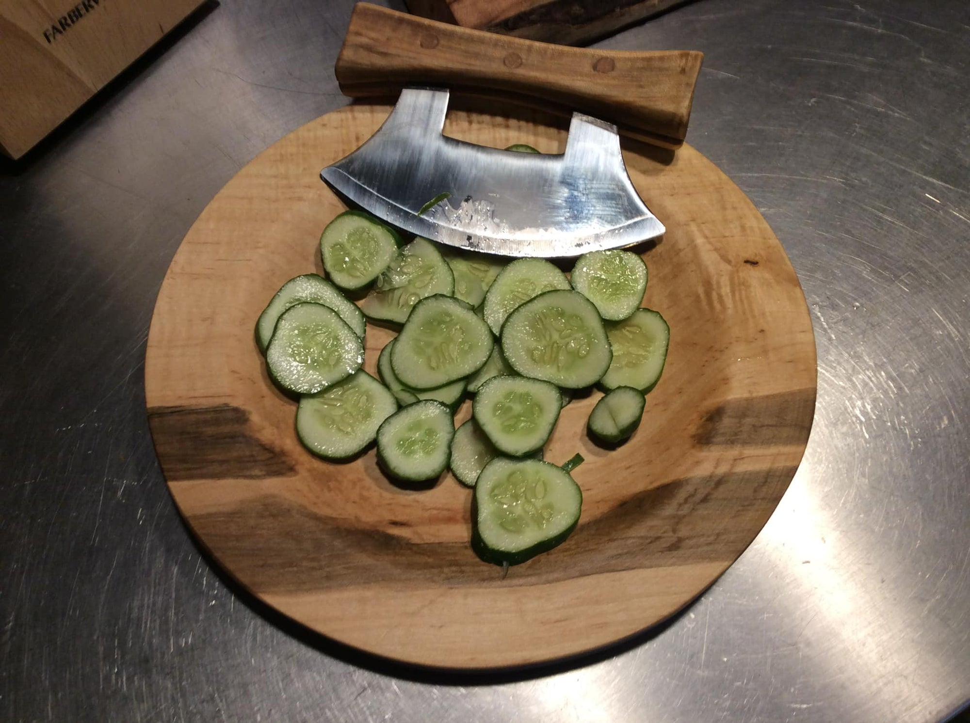 An exquisite Ulu Bowl and Knife with Handmade Handle placed on a wooden plate, accompanied by fresh cucumbers.