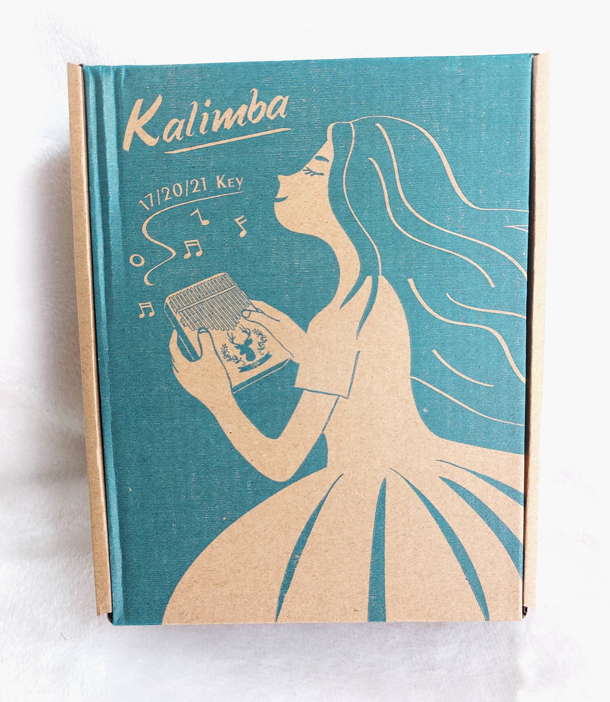 A book-style box with a graphic of a woman playing a Kalimba Musical Instrument, labeled "kalimba 17/21 key," against a teal background.