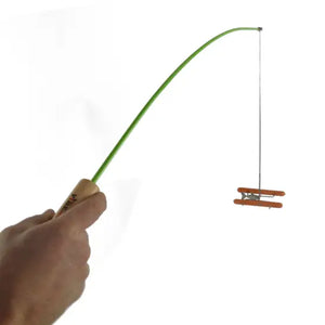 Hand holding a green Fishing Poles roaster with a miniature orange chair dangling on a string from its tip against a white background.