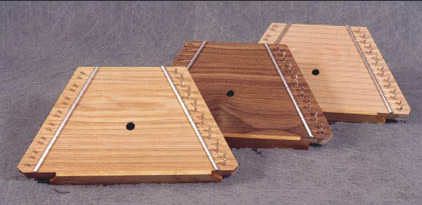 Three wooden triangles alongside a Lap Harp Birch on a gray surface, surrounded by acoustic folk instruments and music cards.