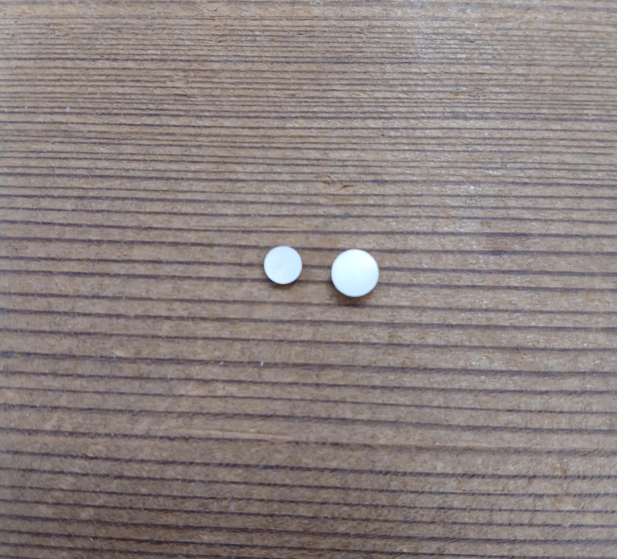 Two small, round white pills lie on a wooden surface, resembling non-installed Mother of Pearl Inlay Dots, with one larger than the other.