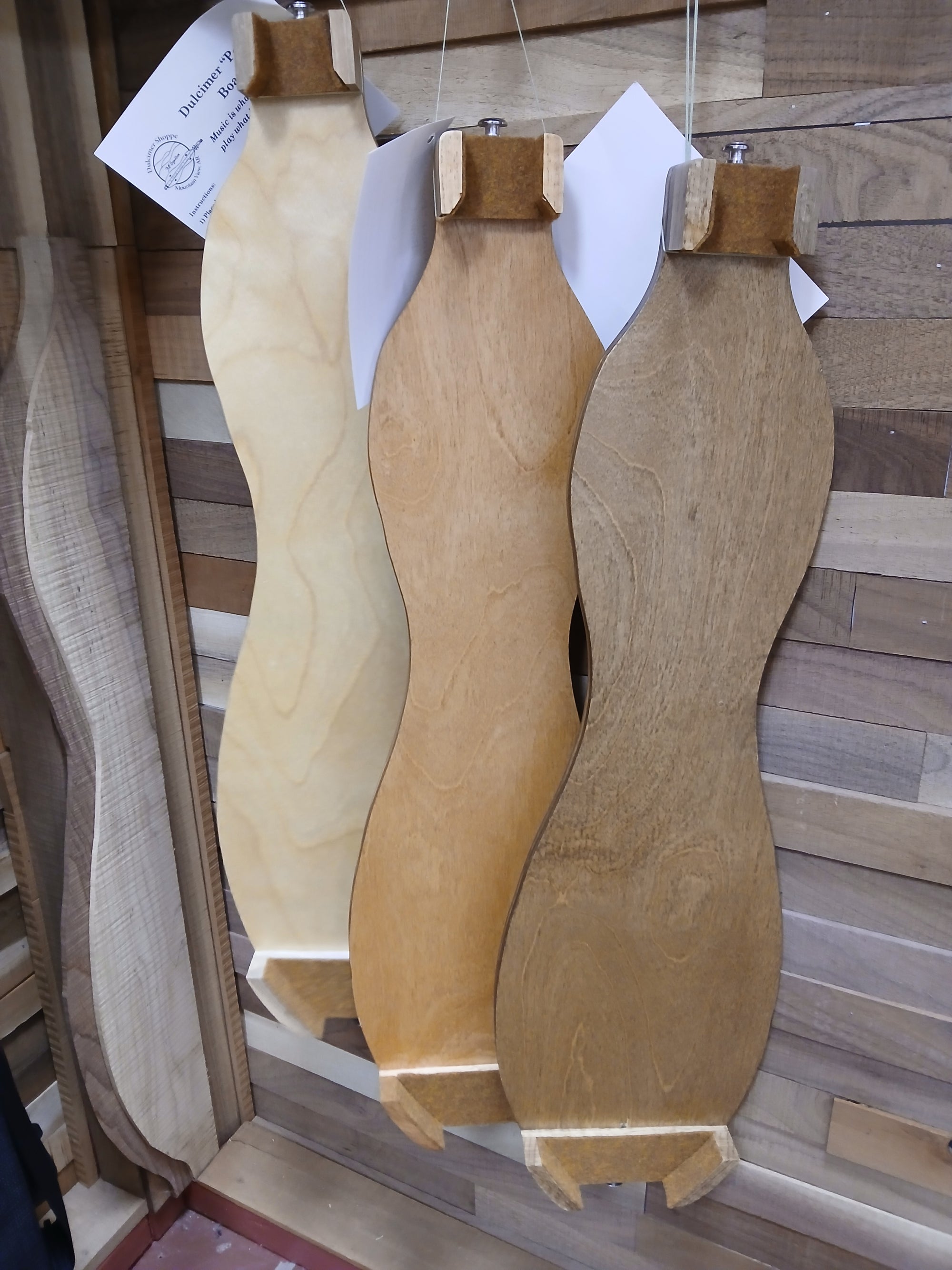 Three Possum Board table legs, each with a slightly different shade, hang vertically in front of a wood-paneled wall.