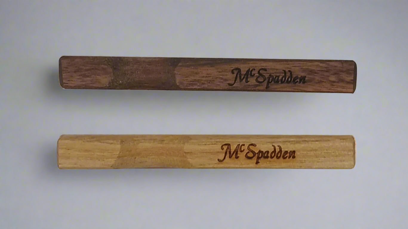 Two handcrafted McSpadden Noters, highlighting the rich hues of their contrasting lighter and darker woods and elegantly engraved with "McSpadden," are set against a plain backdrop.