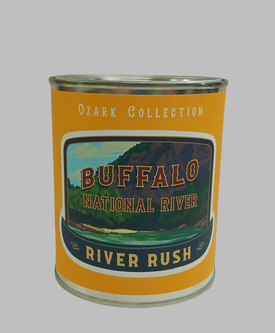 A "River Rush" tin candle from the renowned Ozark Collection, labeled "Buffalo National River," features an illustrated landscape of majestic mountains and a winding river.