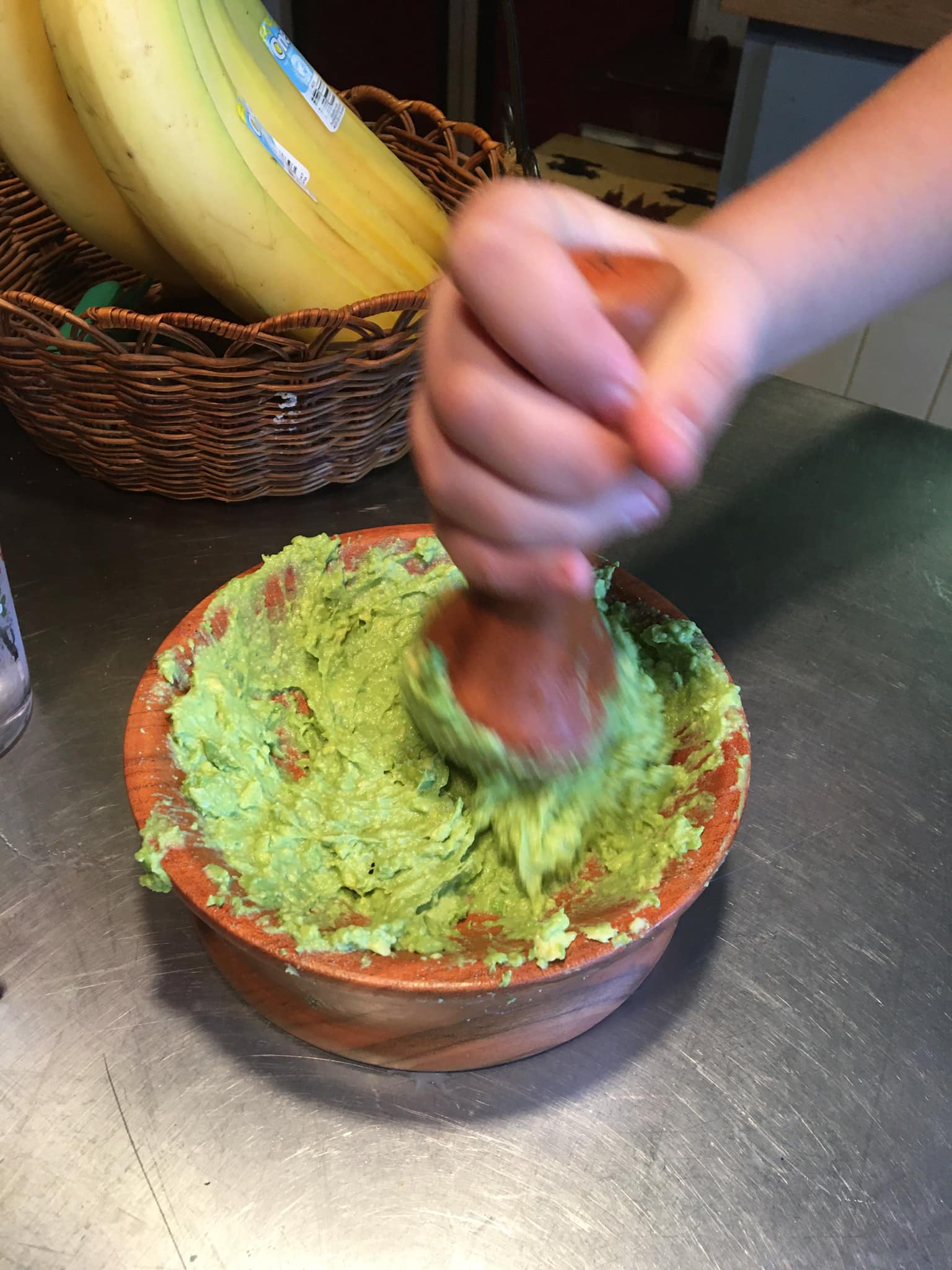 Using a wooden mortar and pestle, a person handcrafts guacamole, utilizing this culinary tool to squeeze the green mixture into a bowl.