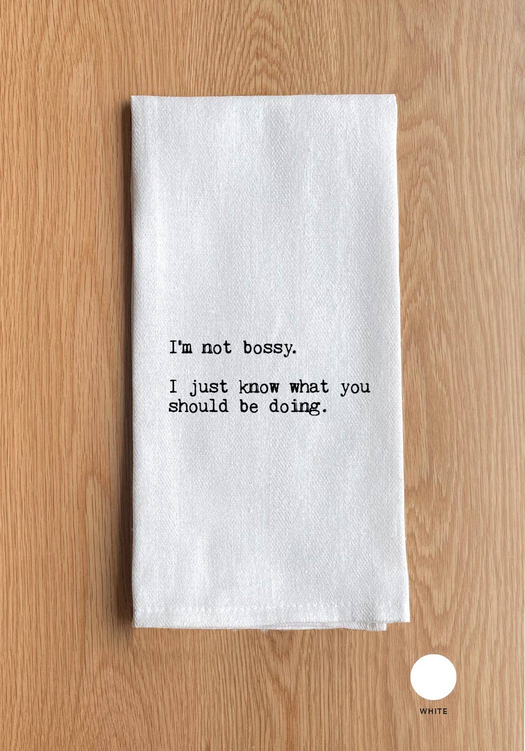 A versatile kitchen towel on a wooden surface with printed text that reads, "I'm not bossy. I just know what you should be doing," from the product line of the same name.