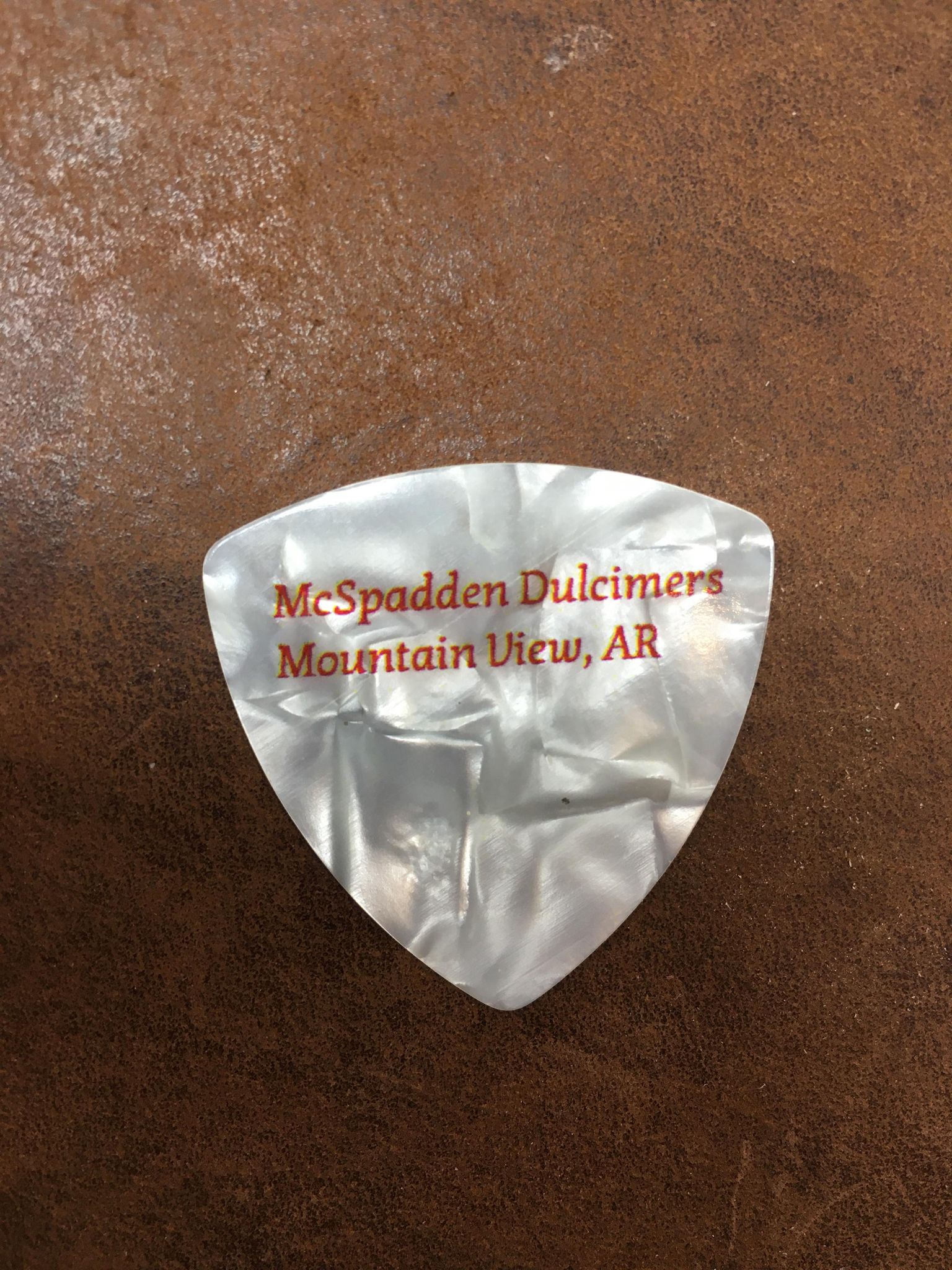 A White Pearloid guitar pick with a label that reads McSpadden Picks.