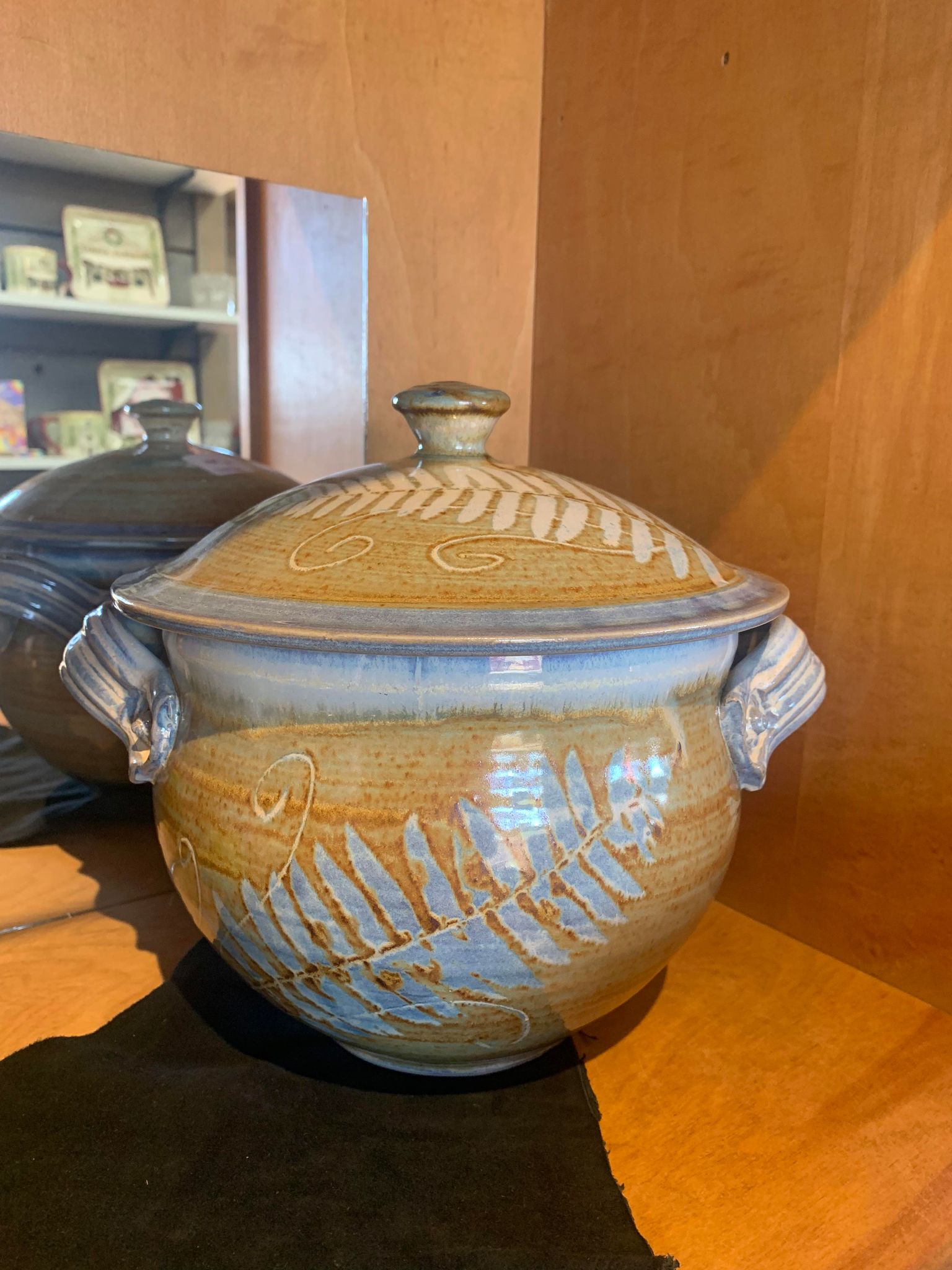A Perry Munn Pottery Fern Casserole Dish with Lid sits on top of a mirror lid.