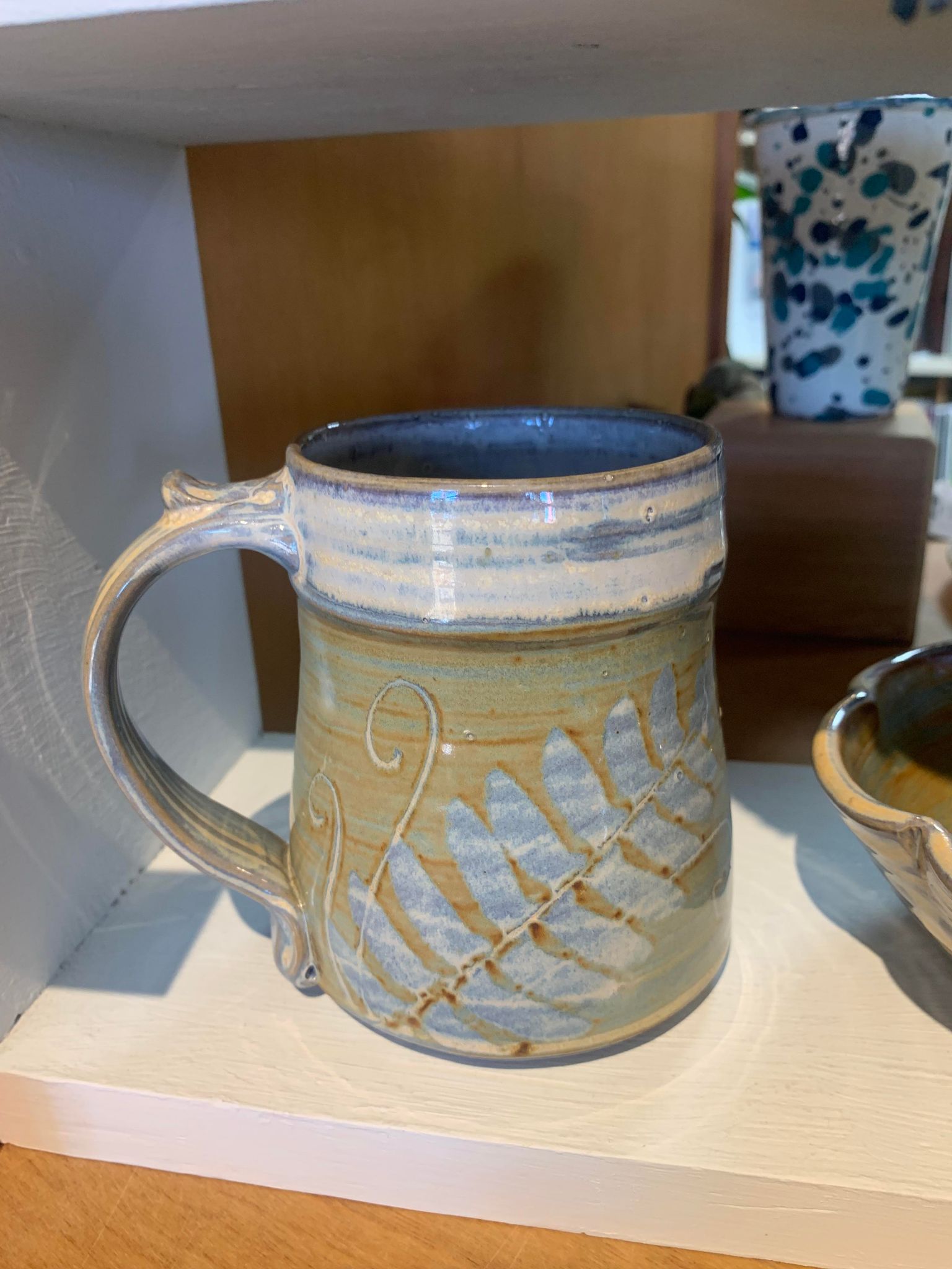 A Perry Munn Pottery Fern Mug sits on a candle holder shelf.
