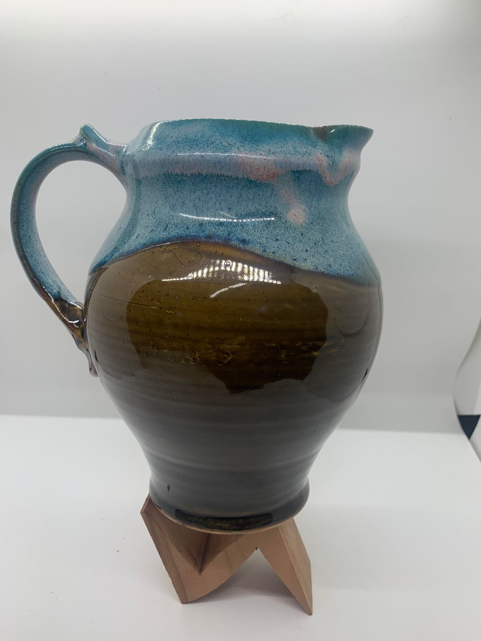 A blue and brown Perry Munn Pottery Large Pitcher on a wooden stand.