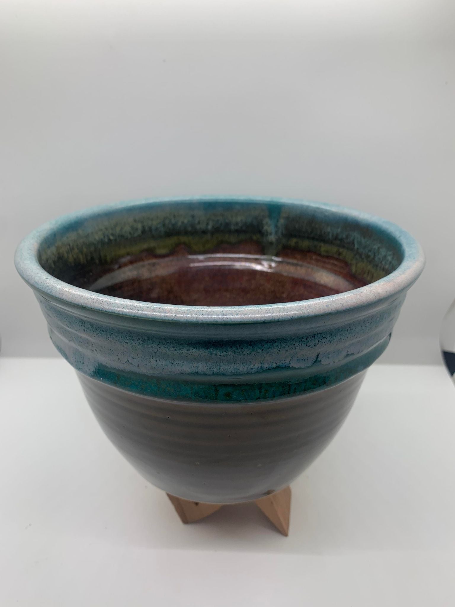 A blue and green Perry Munn Pottery Mixing Bowl on a wooden stand.