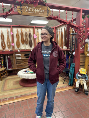 A woman in a maroon Dulcimer Shoppe Hoodies hoodie standing in front of a store.