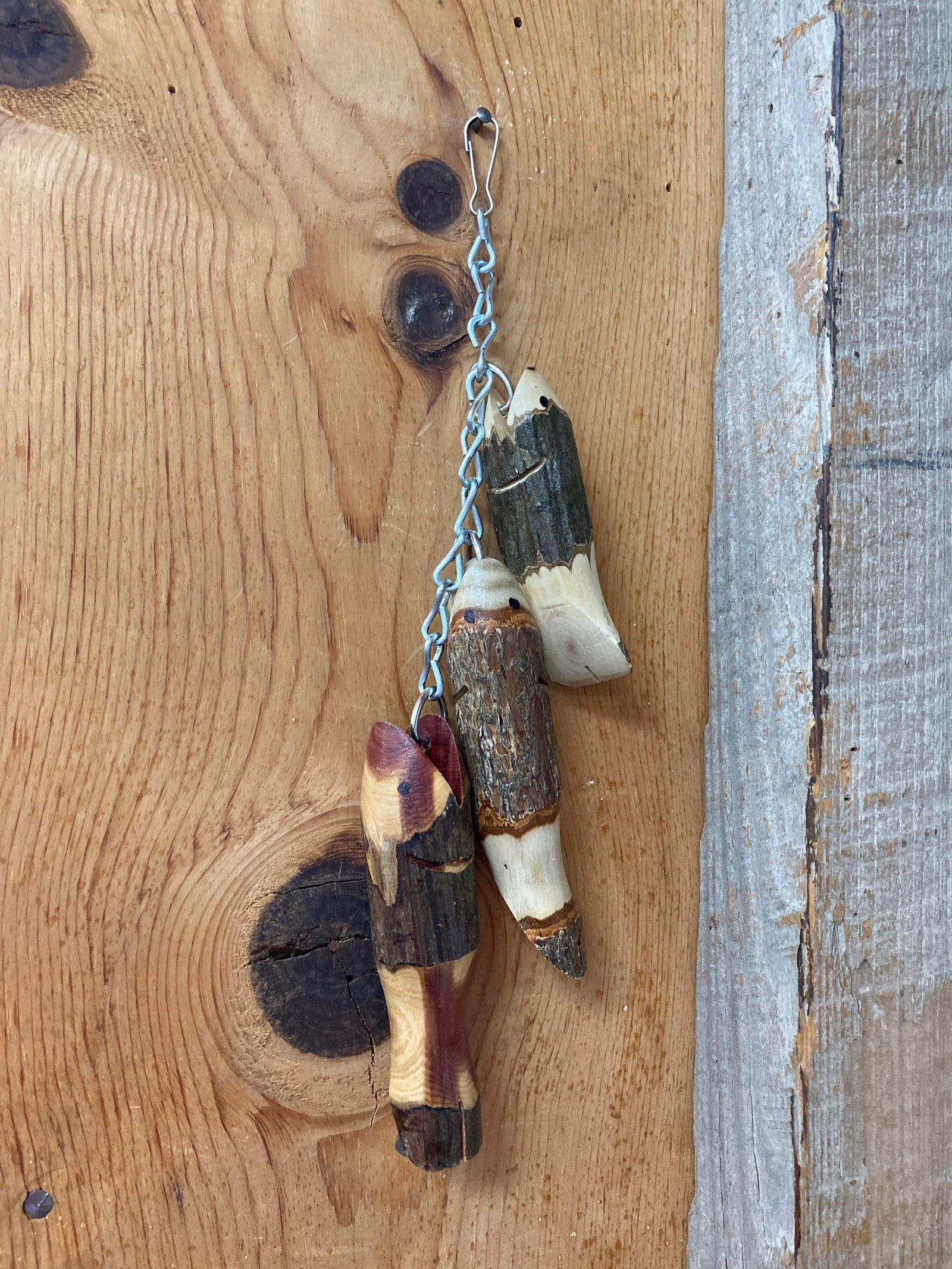 A Fish-Mini Stringer with wooden branches attached to a metal chain, set against a wooden plank background.