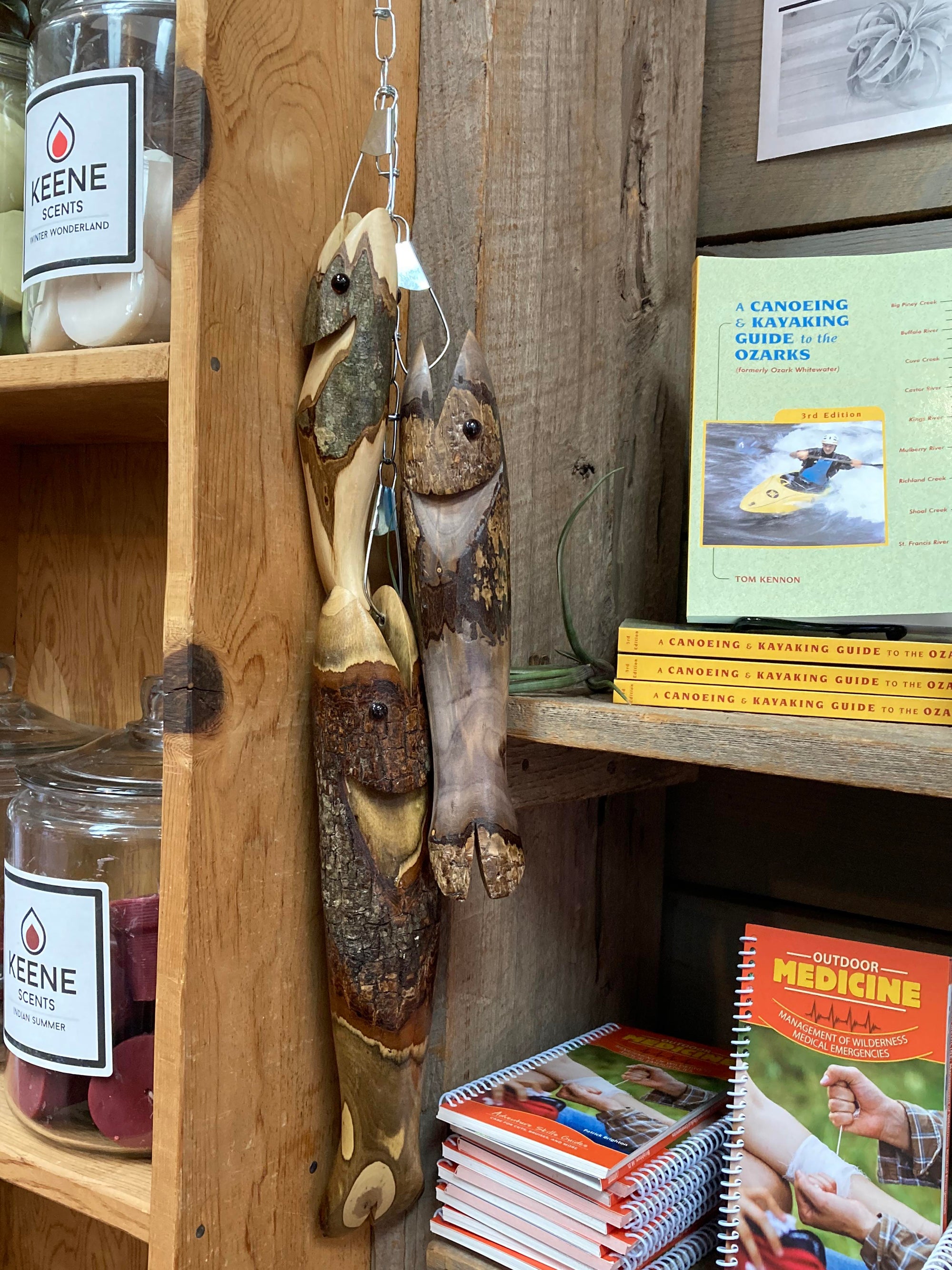 Hand-carved Fish-Stringer of 3 ornaments hanging beside a bookshelf with outdoor and adventure guides, enhancing the cabin décor.