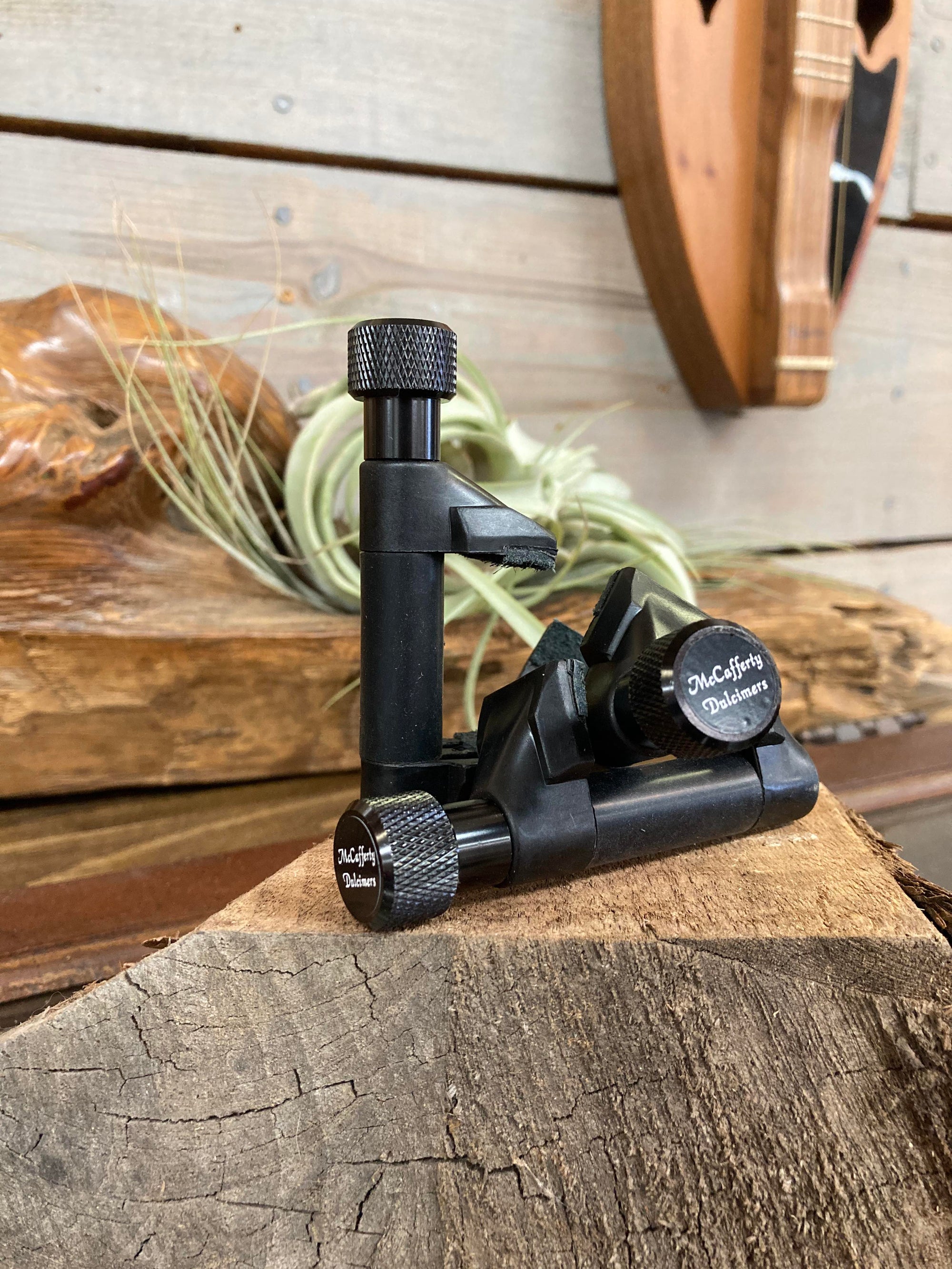 Fly tying vise with a large knob on a wooden surface with decorative greenery in the background, using McCafferty Capos.