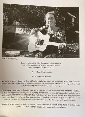 A woman sitting outdoors, smiling gently while playing an acoustic guitar from Song by Song Vol 1 by Aubrey Atwater.