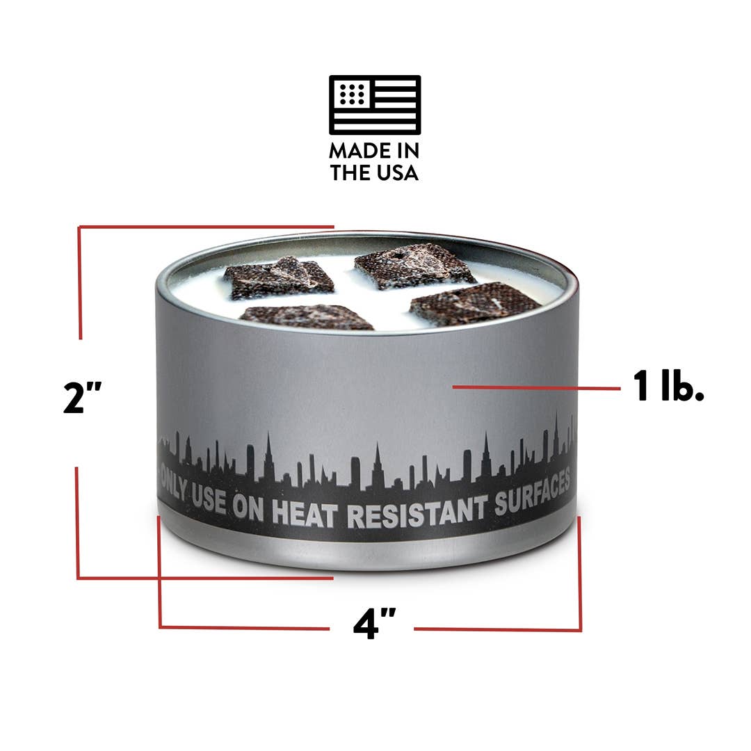 A 1 lb cylindrical candle labeled "Mini Portable Fire Pits - City Bonfires® by Coleman®," featuring a city skyline design and three wicks, measures 4 inches in diameter and 2 inches high.