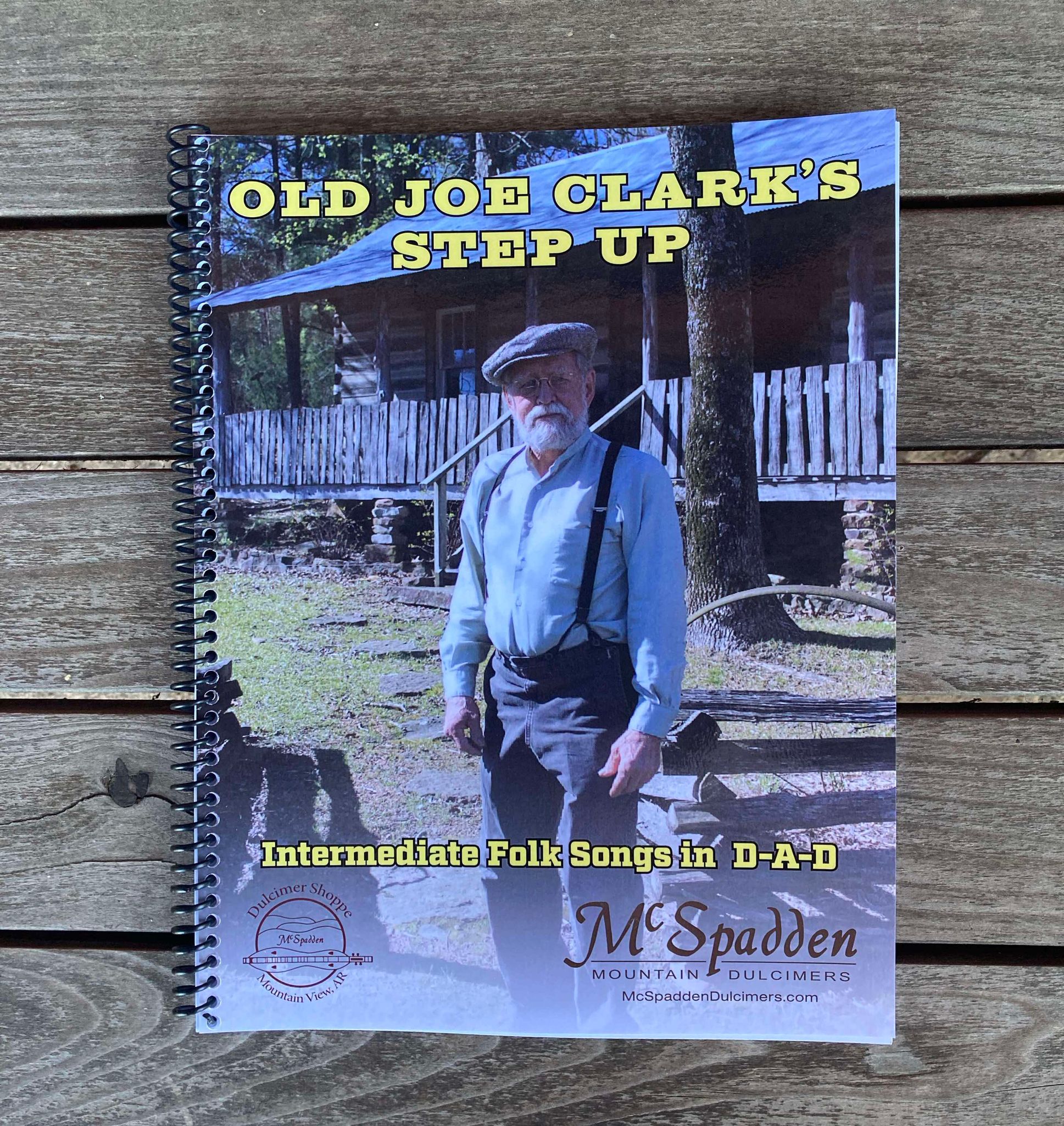 Cover of a book titled "Old Joe Clark's Step Up -by Red Dog Jam," featuring a man in period clothing standing outside a rustic cabin. The subtitle reads, "Intermediate Book of Folk Songs in D-A-D." The book is by McSpadden Mountain Dulcimers.