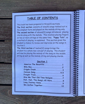 A table of contents page in "Aunt Rhody's Step Up - by Red Dog Jam," a spiral-bound intermediate book, outlining three sections focused on beginning melody, two-string melodies, and note-reading. Section 1 lists page numbers for several folk songs.