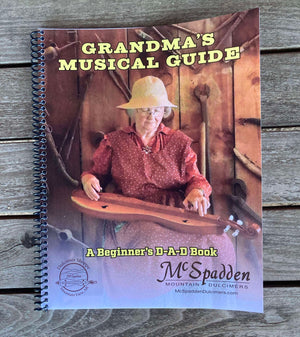 A spiral-bound book titled "Grandma's Musical Guide - by Red Dog Jam" featuring a woman playing a Mountain Dulcimer on the cover, ideal for those starting with D-A-D tuning.