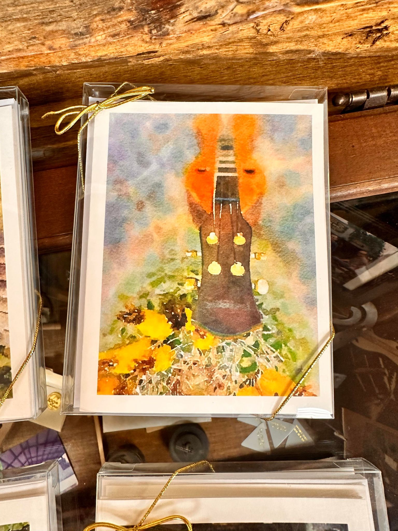 A Dulcimer Greeting Card Set by Ellen Pratt, featuring a watercolor painting of a guitar neck surrounded by yellow flowers and hand drawn by Ellen Pratt, is displayed in a clear plastic cover with a gold tie.