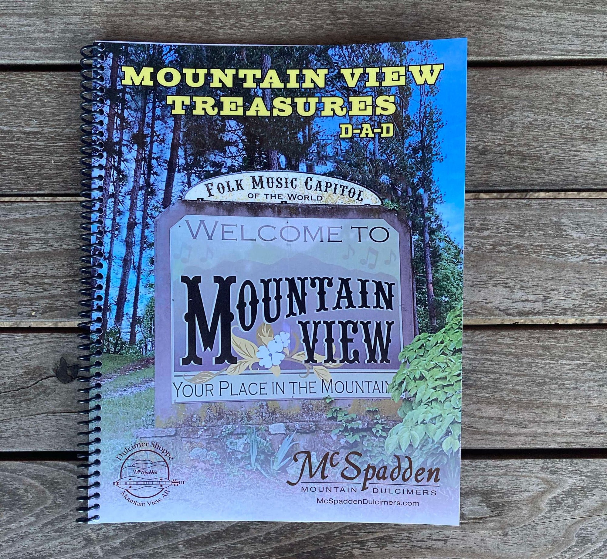 A spiral-bound book titled "Mountain View Treasures - by Red Dog Jam" with a cover illustration welcoming to Mountain View, highlighting it as the "Folk Music Capitol of the World." This edition includes classic tunes like "Songs We Learned in Mountain View" and features a special section on the mountain dulcimer.