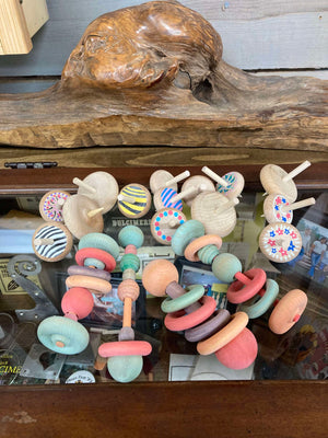 Neil's Wood Shop Toys displays a collection of colorful, handcrafted wooden tops and spinning toys with a vintage design on a wooden shelf.