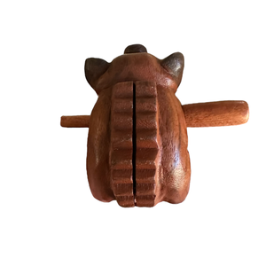 A handmade Wooden Musical Pig Percussion Instrument with carved ridges on its back and a wooden stick through its mouth, shown on a white background.