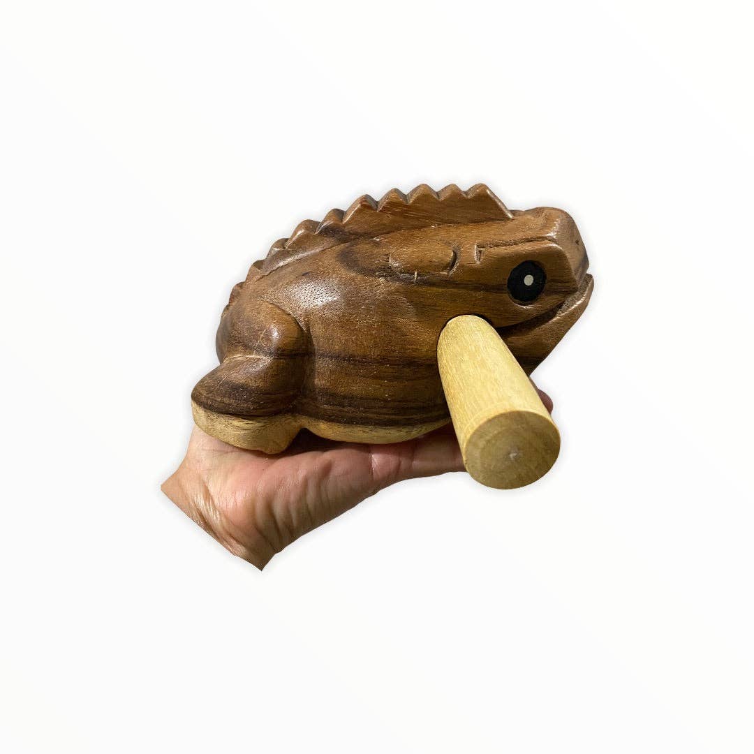 A hand holding a beautifully carved Natural wooden frog with a detachable stick inserted into its mouth, showcasing quality craftsmanship and handmade in Thailand, this unique piece is known for its distinctive croaking sound.