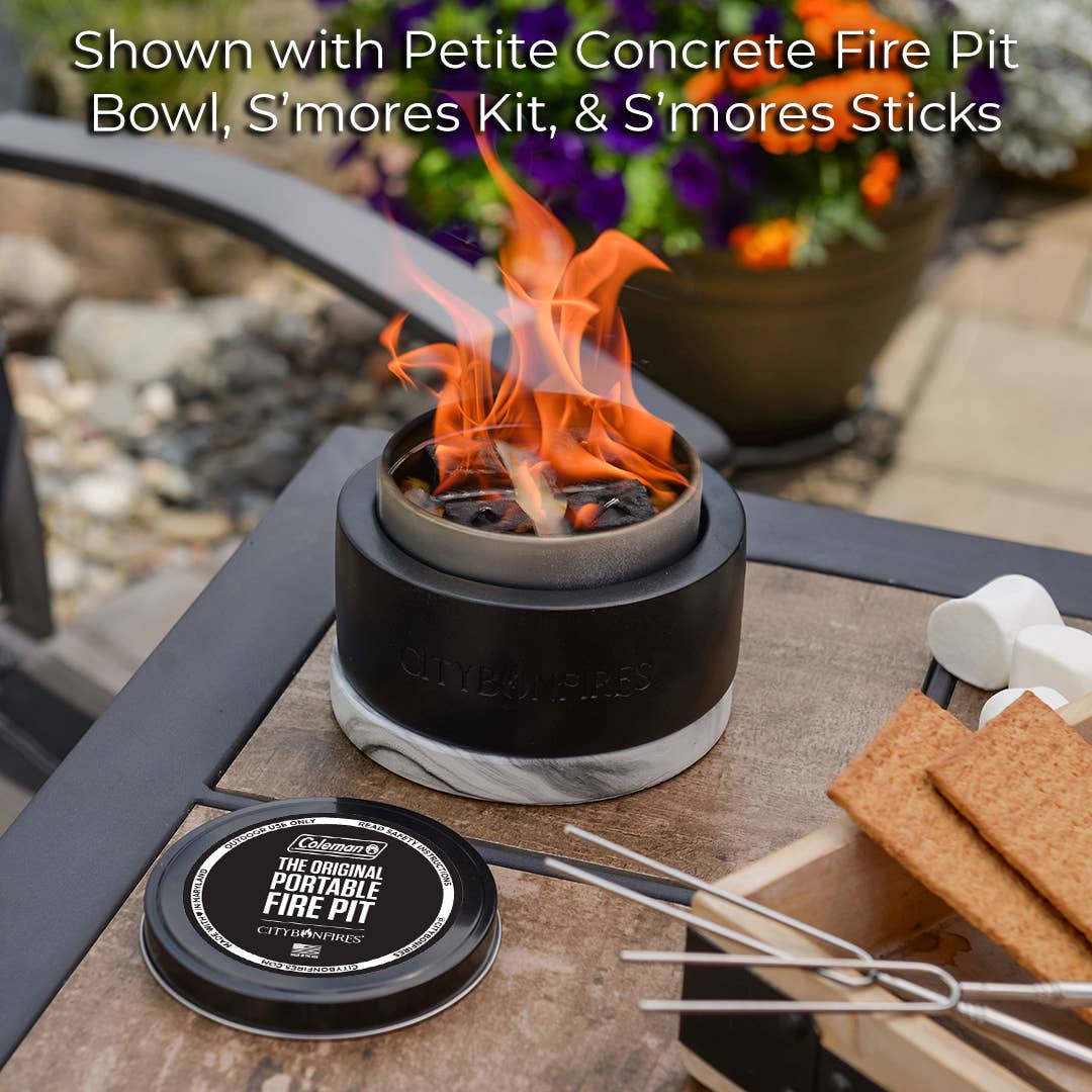 Mini Portable Fire Pits - City Bonfires® by Coleman® on a table with a s'mores kit, including marshmallows, graham crackers, and a chocolate tin, surrounded by purple flowers. Perfect for eco-friendly bonfires.