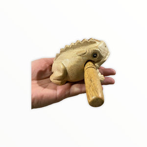 A hand holds the Natural wooden frog, a small wooden croaking frog-shaped instrument, handmade in Thailand, with a detachable stick used for playing.