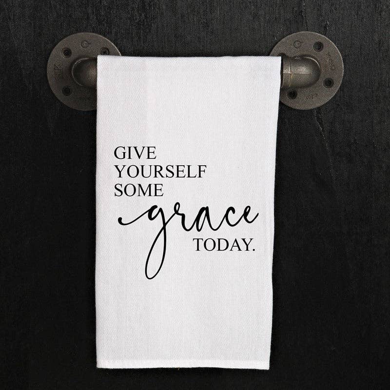 A white, 100% cotton towel from the "Give yourself some grace today" collection hanging on a metal rod with the phrase "Give yourself some grace today." printed on it.