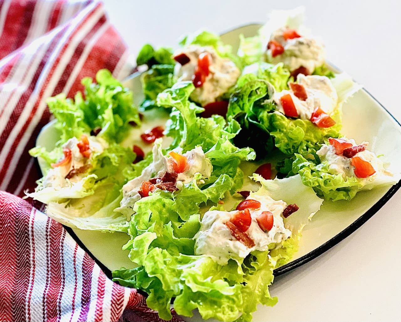 A plate of fresh lettuce leaves topped with BLT Dip Mix made from sour cream, bacon, and diced red tomatoes, set next to a red and white striped cloth napkin.