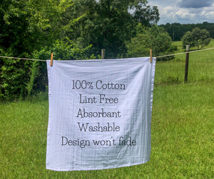 An Arkansas Tea Towel made of 100% cotton hanging on a line in a field.